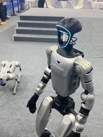 Humanoid robot walking indoors at a venue, a four-legged robot behind it