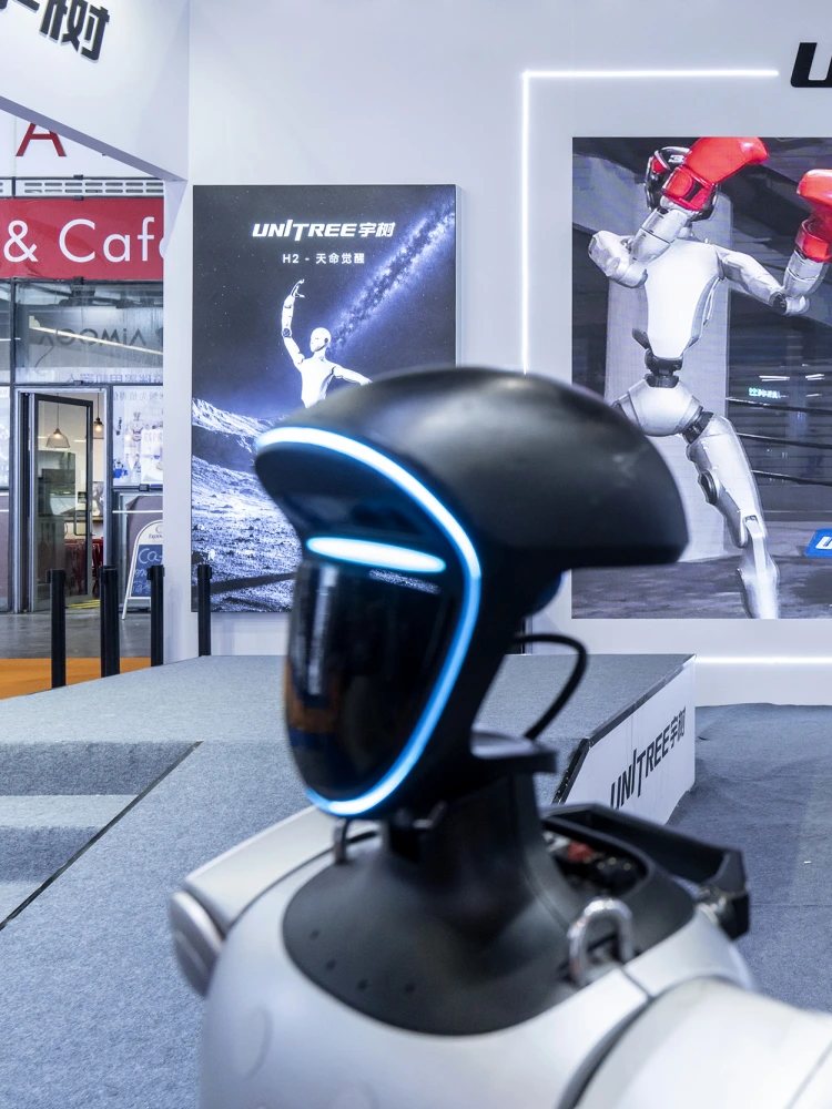 A Unitree exhibition stand with a sparring demonstration on the screen behind