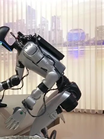 A Unitree humanoid bending to pick something up using whole-body control